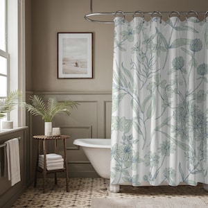 May include: A white shower curtain with a green and blue floral pattern. The shower curtain is hanging in a bathroom with a white bathtub and a brown wooden side table.