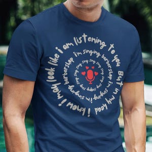 以下が含まれることがあります： 白い円形のデザインが施されたネイビーブルーのTシャツ。テキストは「聞いてるけど、頭の中ではバーバーショップで歌ってるみたい」