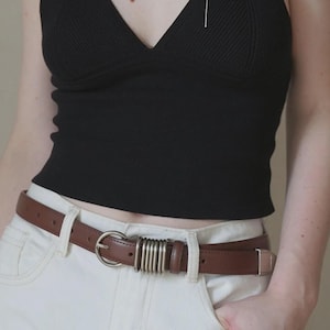 Könnte beinhalten: Ein Set aus drei Keramikbechern mit gesprenkelter, matter Oberfläche. Die Becher sind in Creme-, Hellgrau- und Dunkelgrautönen gehalten. Jeder Becher hat ein schlichtes, minimalistisches Design und einen abgerundeten Henkel.