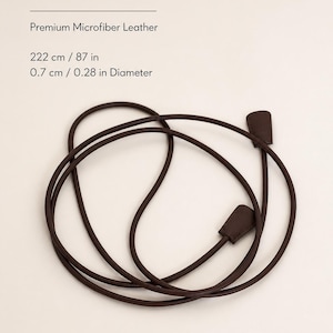 May include: An extra-long wrap belt made of premium microfiber leather. The dark brown cord measures 87 inches in length and 0.28 inches in diameter, featuring two flat, rectangular end pieces. The text reads: EXTRA-LONG WRAP BELT, Premium Microfiber Leather, 222 cm / 87 in, 0.7 cm / 0.28 in Diameter.