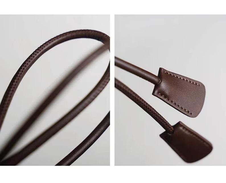 May include: A dark brown leather cord with a smooth, rounded profile and visible stitching along the edges. The cord features two flat, rectangular leather tabs at the ends, each secured with matching brown thread stitching.