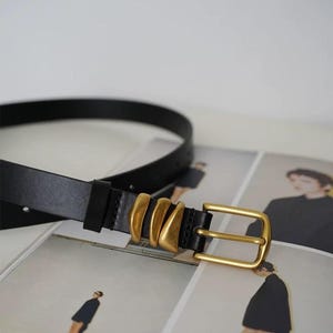 A black leather belt with a gold-tone buckle and three gold-tone decorative loops