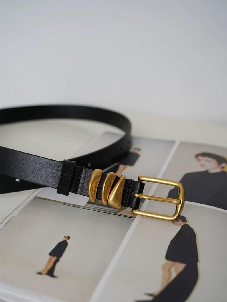 A black leather belt with a gold-tone buckle and three gold-tone decorative loops