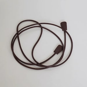 May include: A long, thin, dark brown cord strap with a smooth, rounded texture. The strap features two flat, rectangular-shaped end pieces in a matching dark brown color, securely attached to each end of the flexible, coiled cord.