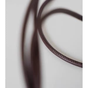 May include: A dark brown, thin, rounded cord with a visible stitched seam running along its length. The cord is flexible and curves in a loop, displaying a smooth, semi-glossy texture on its surface against a plain, light-colored background.