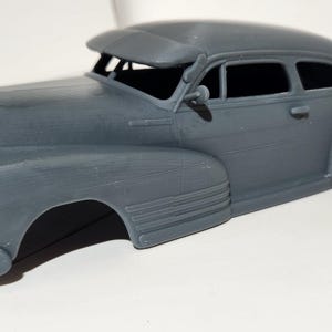 May include: A gray plastic model car, a 1940s era sedan, with no wheels or interior. The car is missing the front bumper and grill.