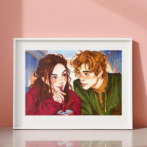Pode incluir: Uma impressão em aquarela emoldurada com duas pessoas compartilhando uma bebida. A mulher tem cabelo castanho e usa um suéter vermelho, enquanto o homem tem cabelo loiro encaracolado e uma jaqueta verde. A obra de arte está em um fundo rosa.