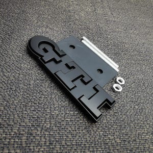 Peut inclure: Emblème noir "GTI" avec matériel de montage. L'emblème est une conception en trois dimensions avec une finition mate. Comprend une plaque de montage noire, deux boulons et deux écrous.