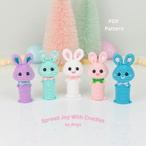Könnte beinhalten: Fünf gehäkelte Fingerpuppen in Form von Hasen in verschiedenen Farben: Lila, Hellblau, Weiß, Rosa und Blau. Die Hasen haben schwarze Augen, rosa Nasen und weißes Garn für ihren Mund. Der Text "Spread Joy With Crochet by Anya" befindet sich unter den Hasen.
