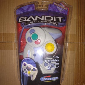 May include: A GameCube controller in its original packaging. The controller is white and gray with colored buttons. The packaging reads "BANDIT" and "Grab the Advantage". The text "The Unfair Advantage" is also visible.