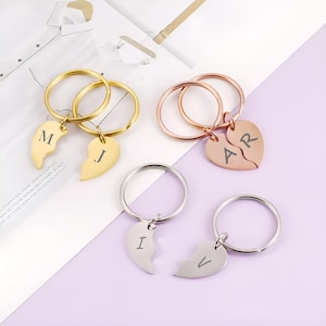 May include: Four keychains with split heart pendants. Two are gold-toned with the letters "M" and "J". One is rose gold with "AR", and two are silver with "I" and "V". Each keychain has a round ring.