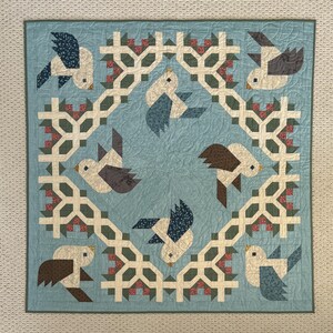May include: A blue and white quilt with a repeating pattern of birds and flowers. The birds are stylized and have a geometric design. The flowers are small and red.