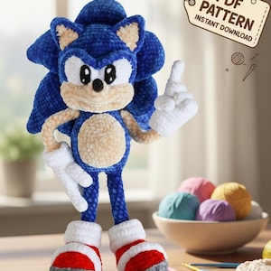 Könnte beinhalten: Eine blaue Sonic the Hedgehog-Puppe aus Häkelarbeit mit weißen Handschuhen und rot-weißen Schuhen. Die Puppe steht mit erhobenem Finger da. Der Text sagt "PDF Pattern Instant Download", "Convenient Crochet Pattern" und "Beginner Friendly!"