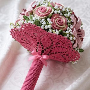 Può includere: Un portafiori all'uncinetto con un design in pizzo rosa, con rose, gigli e piccoli fiori bianchi all'uncinetto. Il manico è rosa pieno. Il testo recita "Crochet Bouquet Holder Pattern" e "PDF Instant Download".