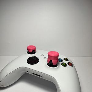 Può includere: Un controller Xbox bianco con due copri-stick rosa.
