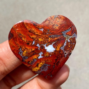 May include: A heart-shaped stone with a striking pattern of red, orange, yellow, and white. The polished surface reveals intricate veining and a natural, earthy texture. This unique piece is a decorative item.