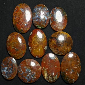 May include: Ten oval-shaped, polished agate cabochons with a variety of red, brown, and white patterns. The cabochons are arranged in a pyramid shape.