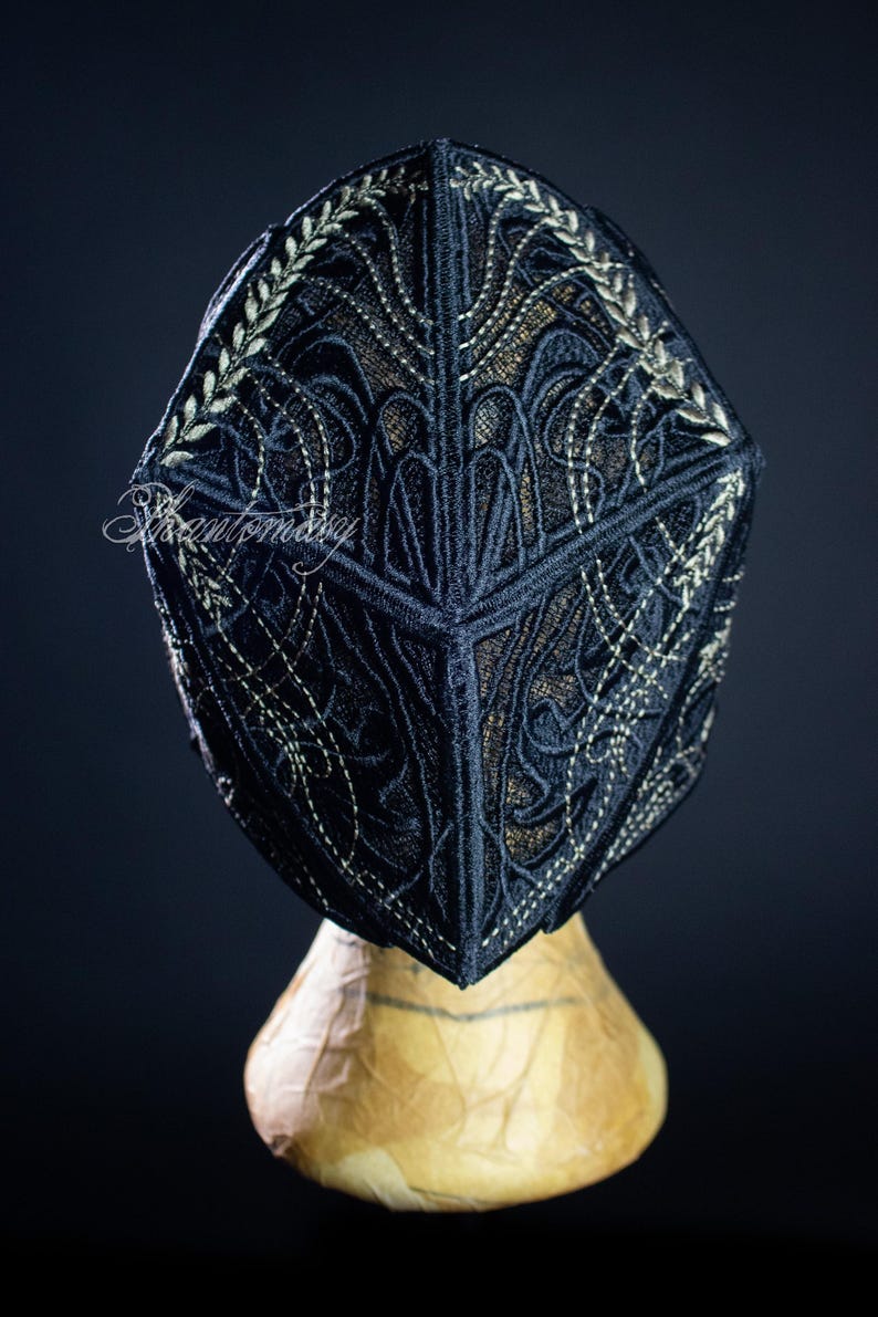 May include: A black cap with intricate embroidered detailing in a gold color. The cap is displayed on a mannequin head against a dark background. The embroidery features floral and geometric patterns.