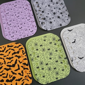 May include: Five rectangular plastic organizers with rounded corners, each featuring a unique Halloween-themed pattern. The designs include purple ghosts, black spiderwebs, orange bats, green skulls and ghosts, and white pumpkins and witch hats.