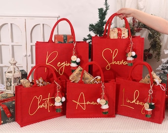 May include: Five red tote bags with gold cursive names: Regina, Shavo, Christina, Amanda, and Lindsay. Each bag has a matching handle and a decorative keychain. The bags are filled with wrapped gifts, perfect for holiday gifting.