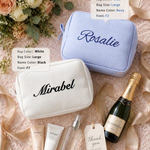 May include: Two large rectangular zippered pouches with a textured waffle pattern. One pouch is light blue with the name Rosalie embroidered in navy blue script. The other is white with the name Mirabel embroidered in black script. Text boxes show customization details.