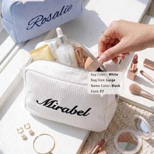 May include: A large white waffle-textured cosmetic bag with the name Mirabel embroidered in black, and a large blue waffle-textured cosmetic bag with the name Rosalie embroidered in navy. The white bag is open, containing various skincare bottles.