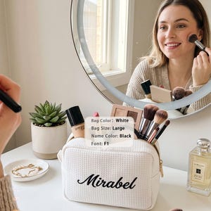 May include: A large white waffle-textured cosmetic bag with a gold zipper, featuring the name Mirabel embroidered in black script font. The bag is filled with various makeup brushes and bottles, and includes a label stating Bag Color: White, Bag Size: Large, Name Color: Black, Font: F1.