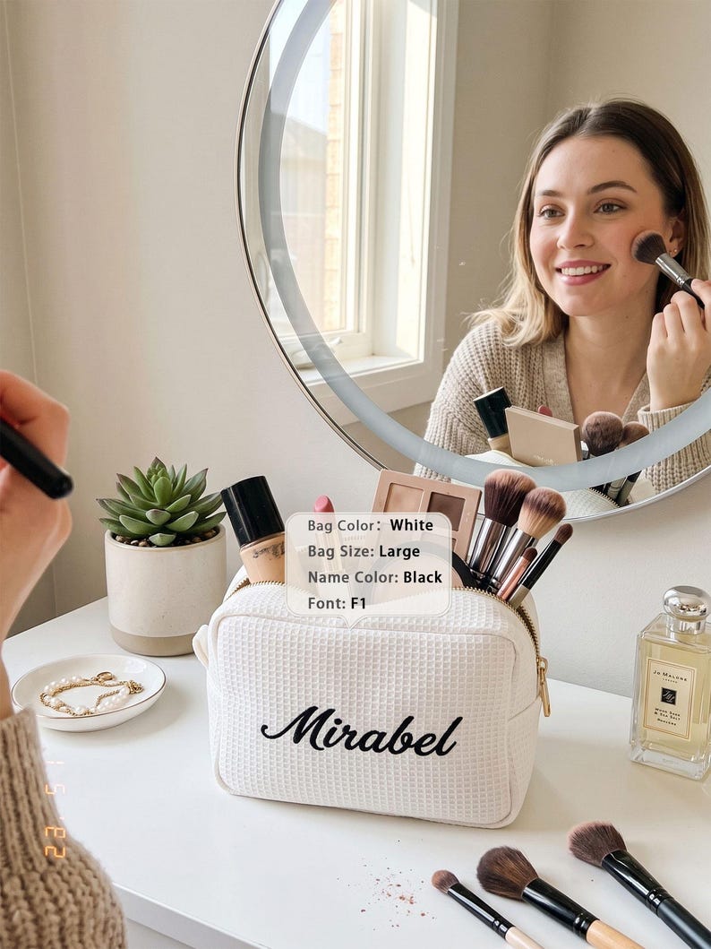 May include: A large white waffle-textured cosmetic bag with a gold zipper, featuring the name Mirabel embroidered in black script font. The bag is filled with various makeup brushes and bottles, and includes a label stating Bag Color: White, Bag Size: Large, Name Color: Black, Font: F1.