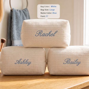 May include: Three large white waffle-textured cosmetic bags with blue embroidered names. The top bag features the name Rachel, while the two bottom bags feature the names Ashley and Bailey. Each bag has a rectangular shape and a zipper closure.
