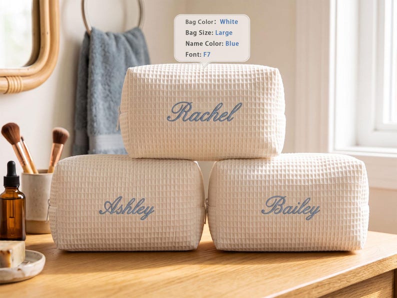 May include: Three large white waffle-textured cosmetic bags with blue embroidered names. The top bag features the name Rachel, while the two bottom bags feature the names Ashley and Bailey. Each bag has a rectangular shape and a zipper closure.