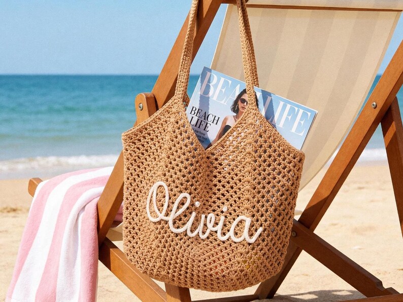 May include: A tan crochet tote bag featuring an open-weave design and two shoulder straps. The front of the bag displays the name Olivia in white, raised, cursive lettering. The bag is constructed from a textured, woven material.