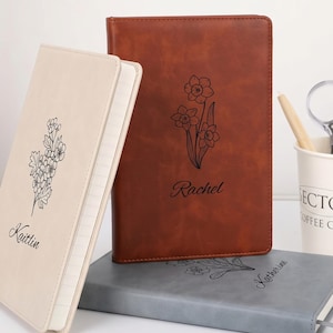 May include: Three rectangular notebooks with smooth covers in cream, brown, and gray. Each notebook features a black line-art floral illustration and a personalized name in cursive script: Kaitlin on the cream, Rachel on the brown, and Katherine on the gray.