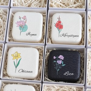 May include: Four square jewelry boxes in white and black, each featuring a unique floral illustration and a printed name. The boxes are displayed in individual white gift boxes filled with shredded paper filler for protection and presentation.