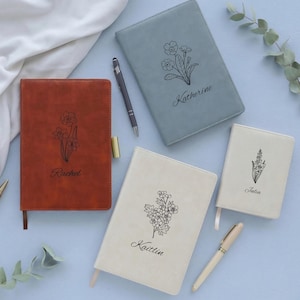 May include: Four rectangular journals in rust, slate blue, and cream colors, each featuring a unique black line-art floral illustration and a personalized name: Rachel, Katherine, Kaitlin, and Julia. Two pens are included with the notebooks.