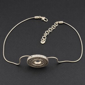 Puede incluir: Una pulsera de plata de ley con un colgante circular central que presenta intrincados patrones grabados. La cadena es de estilo serpiente, equipada con un cierre de mosquet&oacute;n, una cadena extensora ajustable y un peque&ntilde;o dije en forma de coraz&oacute;n con el sello 925.