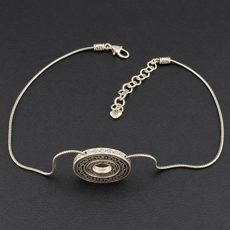Puede incluir: Una pulsera de plata de ley con un colgante circular central que presenta intrincados patrones grabados. La cadena es de estilo serpiente, equipada con un cierre de mosquet&oacute;n, una cadena extensora ajustable y un peque&ntilde;o dije en forma de coraz&oacute;n con el sello 925.