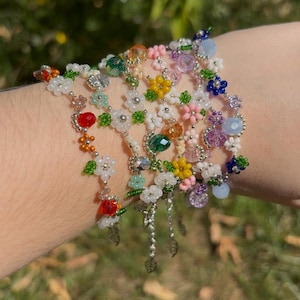 Könnte beinhalten: Mehrere Armbänder mit bunten Blumenmustern. Die Armbänder zeigen rote, orangefarbene, gelbe, grüne, weiße, rosa und blaue Blumen. Einige Armbänder haben baumelnde Blattanhänger.