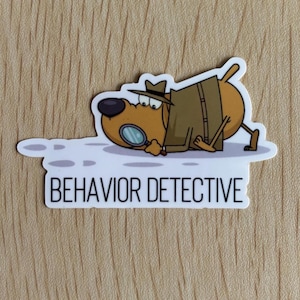 May include: A sticker featuring a cartoon dog dressed as a detective, wearing a hat and trench coat, examining something with a magnifying glass. The text "BEHAVIOR DETECTIVE" is below the dog in a white rectangle.