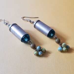 May include: A pair of silver bullet earrings with blue and green beads hanging from them.