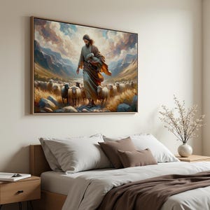 Puede incluir: Una impresión artística en lienzo enmarcada representa una figura con túnicas sosteniendo un cordero, caminando entre un rebaño de ovejas. La obra de arte presenta un paisaje con montañas, un cielo nublado y tonos cálidos. El marco es de color marrón claro.