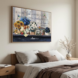 Op de afbeelding: Een ingelijste print met een houten achtergrond, met de tekst "Zegen het voedsel voor ons, de familie naast ons en de liefde tussen ons." Het kunstwerk toont zonnebloemen, kolibries en decoratieve elementen, met het woord "Amen" onderaan.