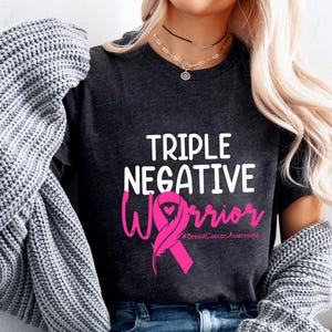 A woman wearing a black t-shirt with the text "Triple Negative Warrior #BreastCancerAwareness" printed on it.