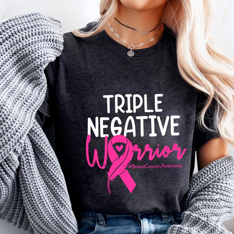 A woman wearing a black t-shirt with the text "Triple Negative Warrior #BreastCancerAwareness" printed on it.