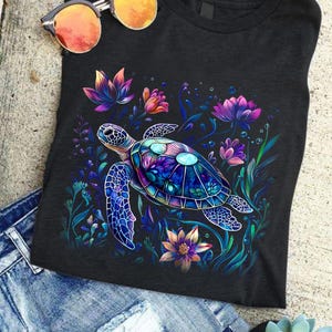 May include: A dark blue t-shirt with a colorful, detailed illustration of a sea turtle swimming through a field of flowers. The turtle is surrounded by purple, blue, and pink flowers.