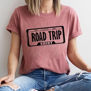 A person wearing a pink t-shirt with the text "OFFICIAL ROAD TRIP SHIRT" printed on it.