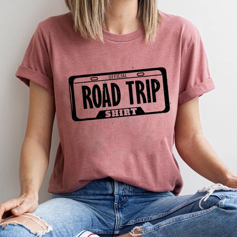 A person wearing a pink t-shirt with the text "OFFICIAL ROAD TRIP SHIRT" printed on it.