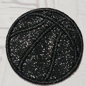 May include: A round, black basketball patch with a glittery finish. The patch features the classic lines of a basketball design. This patch is suitable for various crafting projects, such as decorating clothing or accessories.