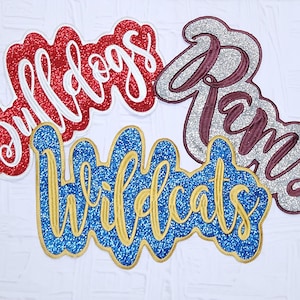 May include: Four glittery team name patches: "Bulldogs" in red and white, "Rams" in silver and maroon, and "Wildcats" in blue and gold. These patches are ideal for sports fans and can be used to personalize apparel or accessories.