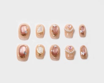 May include: Set of ten false nails with a pink and gold design. Each nail features a different design with a pink stone, gold accents, and white butterflies or pearls.