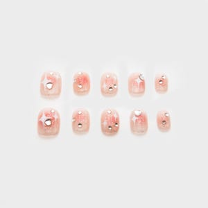 Puede incluir: Diez uñas postizas para los dedos de los pies de color rosa y blanco con purpurina plateada y pedrería.